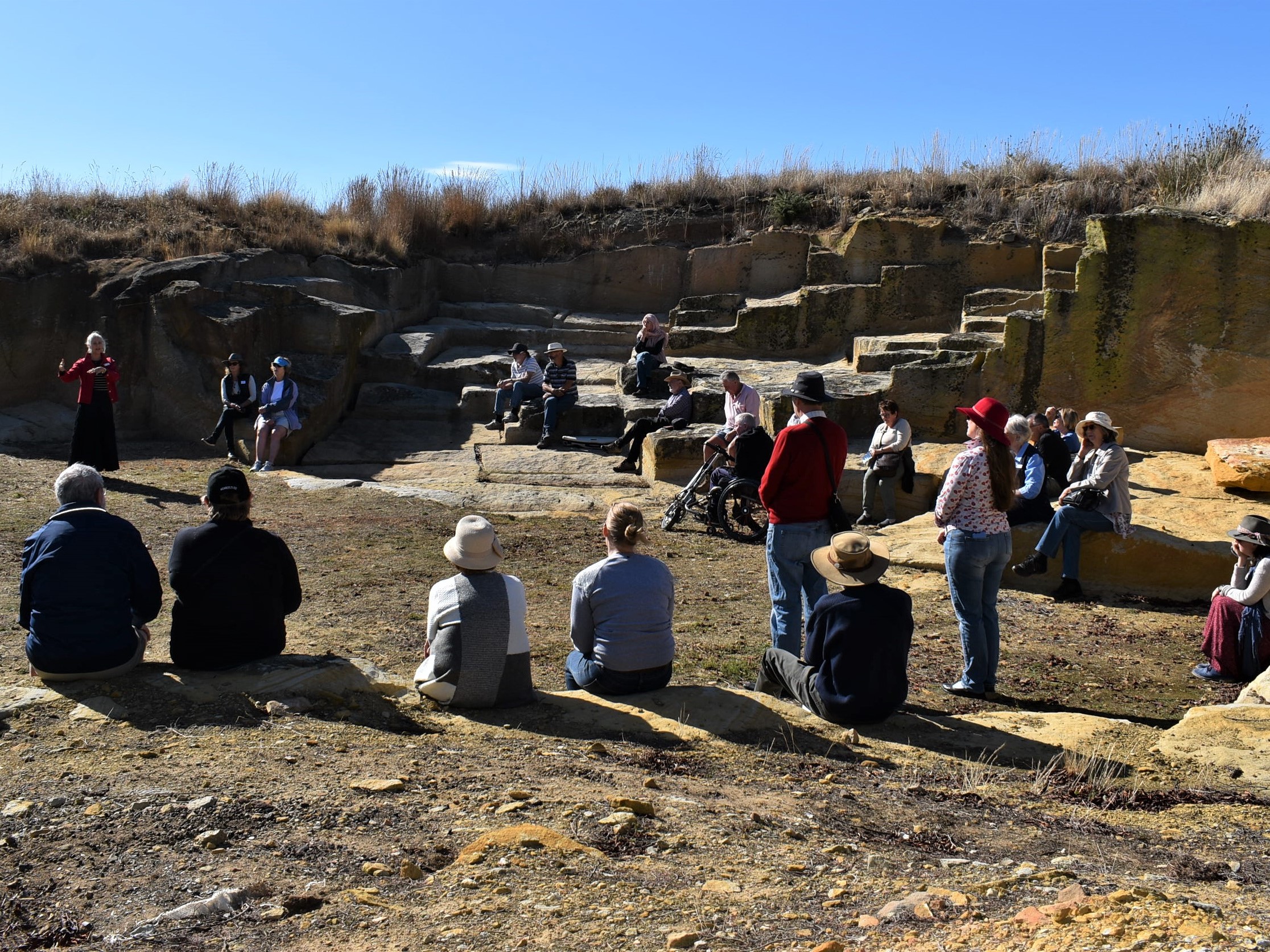 Photo of tour guide giving a talk to a group of people sitting around the Ross Quarry.